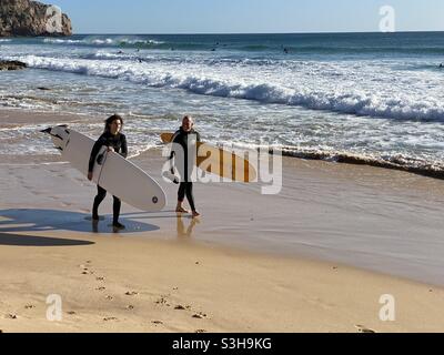 Due surfisti che camminano lungo la spiaggia di Praia do Zavial nell'Algarve in Portogallo Foto Stock