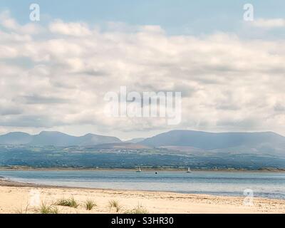 Vista di Snowdonia attraverso lo stretto di Menai dalla spiaggia a Newborough Warren, Anglesey, Galles del Nord, Regno Unito Foto Stock