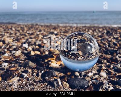 Palla di vetro trasparente su una spiaggia di ciottoli Foto Stock