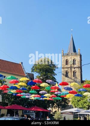 Settembre 2021, nella città tedesca di Ibbenbüren, molti ombrelloni colorati appendono steso attraverso la piazza del mercato in bel tempo e cielo blu. Foto Stock