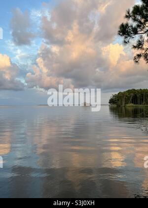Le spettacolari nuvole al tramonto si riflettono sulle calme acque della baia Foto Stock