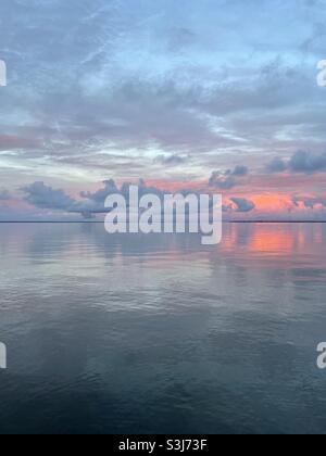 Nuvole di tramonto rosa brillante che si riflettono su calme acque di baia Foto Stock