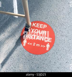 Mantenere la vostra distanza 2 metri covid sicuro distanziamento rosso cartello pavimento Foto Stock