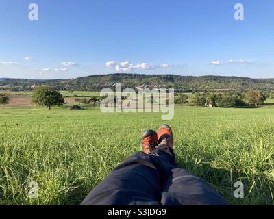 Gambe e piedi di escursionista fare una pausa su un prato in idilliaco paesaggio rurale nella Germania meridionale Foto Stock