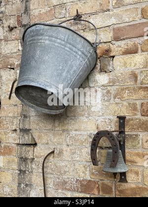 Secchio di metallo, ferro di cavallo e un piccolo campanello su un muro di mattoni Foto Stock