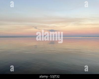 Le nuvole colorate e morbide al tramonto si riflettono sulle calme acque della baia Foto Stock