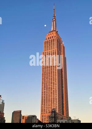 La luna e la città di New York - la luce del mattino presto proietta un bagliore rosa sull'Empire state Building. Foto Stock