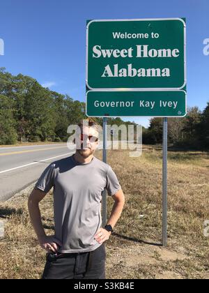Un uomo si trova accanto al cartello della linea di stato dell'Alabama Foto Stock