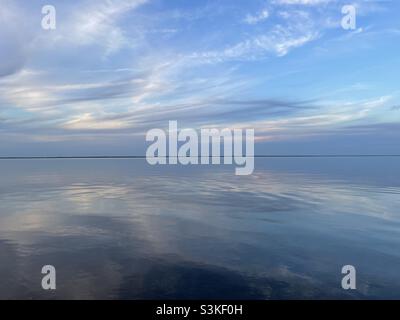 Le nuvole di tramonto si riflettono sulle calme acque della baia Foto Stock