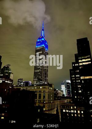 Luci blu brillante sulla cima dell'Empire state Building contro un cielo grigio nuvoloso a New York City Foto Stock