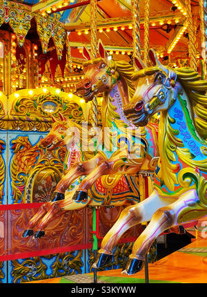 Tre cavalli attendono i cavalieri su una giostra di allegro giro in un terreno fieristico. Si tratta di una scena vivace e colorata, ricca di emozioni per l'infanzia! Foto ©️ COLIN HOSKINS. Foto Stock