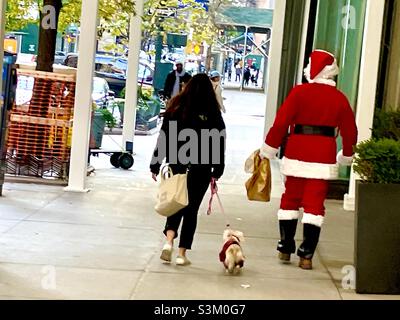 Babbo Natale e i suoi Helpers, una donna e il suo cane, camminano per le strade di New York Foto Stock