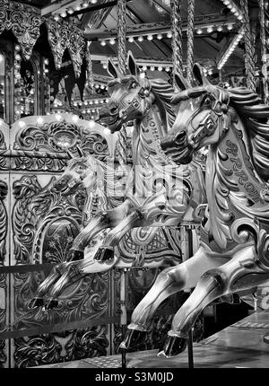 Tre cavalli attendono i cavalieri durante un giro in giostra Merry Go Round in una fiera divertente. Un'immagine monocromatica ad alto contrasto. Ricordi dell'infanzia. Foto ©️ COLIN HOSKINS. Foto Stock