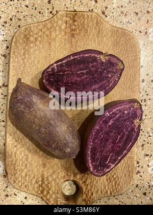 Patate dolci viola su un tagliere in cucina. Foto Stock