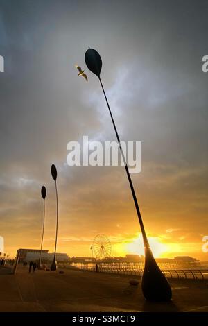Sculture di erba di mare che si piegano nel vento sulla passeggiata di Blackpool con molo centrale sullo sfondo. Foto Stock