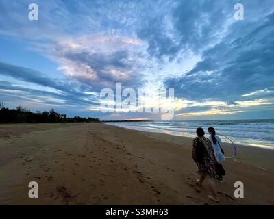 Una donna e sua figlia camminano sulla spiaggia al tramonto Foto Stock