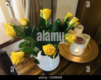 Rose gialle vibranti in un vaso bianco accanto alle candele e un bruciatore di cera fusa Foto Stock