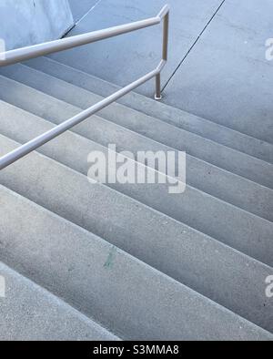 Passi di cemento all'aperto, con un corrimano metallico al centro, presi ad un angolo per aggiungere un certo interesse astratto. Foto Stock
