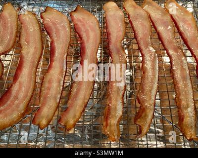 Rashers di pancetta su una rastrelliera sopra foglio di alluminio, dopo cottura nel forno Foto Stock