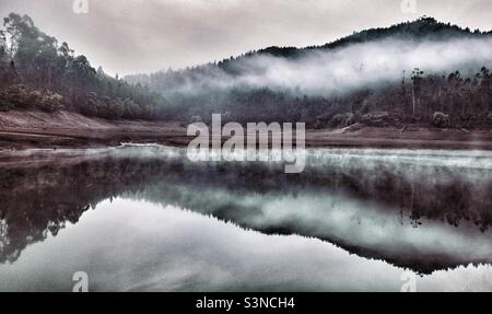 La nebbia del mattino presto pende sulle colline alberate e si riflette nel fiume Foto Stock