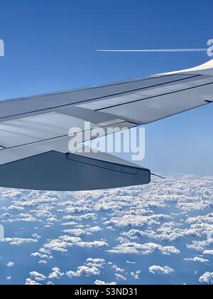 Alettone che vola su nuvole bianche con un altro aereo in lontananza lasciando un jet trail Foto Stock