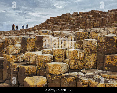 I turisti/visitatori camminano sulle uniche formazioni rocciose di basalto che formano l'area conosciuta come Selciato del Gigante ad Antrim, Irlanda del Nord. Le strutture esagonali sono state formate 60 milioni di anni fa. ©️ CH Foto Stock