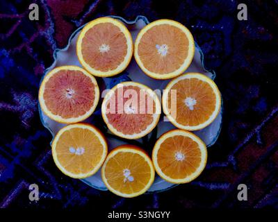 Arance fresche e succose, disposte in cerchio. Pieno di vitamina C. scuro, tappeto orientale come sfondo. Otto metà. Foto Stock