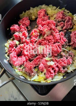 Primo piano di carne cruda macinata fritta in una padella su un piano di stufa residenziale, 2022, USA Foto Stock