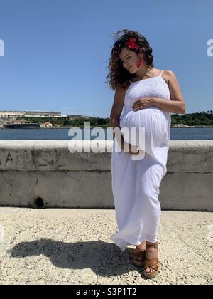 La donna incinta di otto mesi carezza teneramente il suo ventre crescente a l'Avana Vecchia, l'Avana, Cuba, Caraibi. Aspettative di maternità. Foto Stock