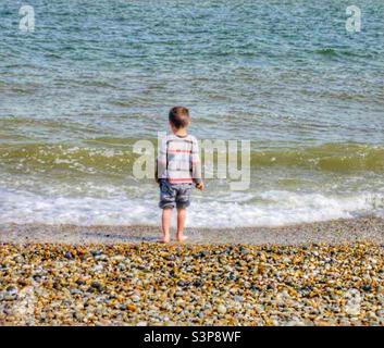 Little Boy lanciano pietre nel mare Foto Stock