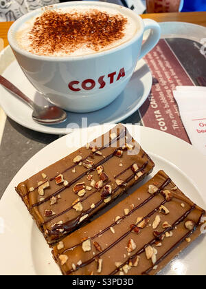 Un caffè cappuccino e una fetta di torta in un caffè Costa. Foto Stock