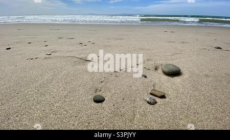 Piccoli ciottoli su una spiaggia di sabbia incontaminata con onde che si infrangono sull'Oceano Pacifico e lontane isole visibili sullo sfondo, California Foto Stock