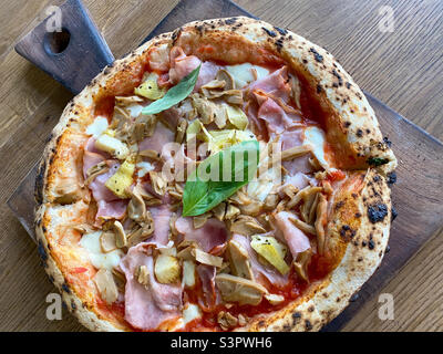 Deliziosa pizza Capriciosa composta da pomodori, mozzarella, prosciutto, funghi marinati, carciofi, basilico e burro. La pizza è fatta nel forno Foto Stock