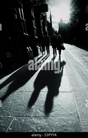 Le persone che camminano lungo il Royal Mile a Edimburgo sono retroilluminate dal sole nel tardo pomeriggio e gettano lunghe ombre Foto Stock