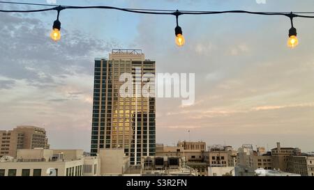 LOS ANGELES, CA, GIUGNO 2021: Nuovo edificio di appartamenti a più piani nel centro città con le nuvole al tramonto e la luce che si riflette sulle finestre. Serie di lampadine in primo piano, parte superiore dell'immagine Foto Stock