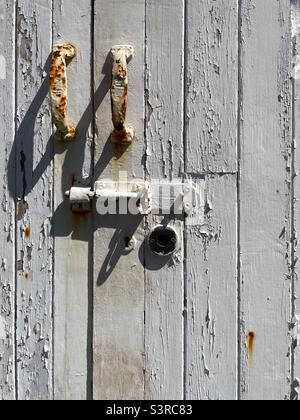 Vecchia porta in legno con vernice bianca sfaldante e maniglie e serratura arrugginite. Foto Stock