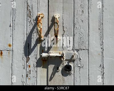 Vecchia porta in legno con vernice bianca e spellante, maniglie e chiavistello arrugginiti. Foto Stock