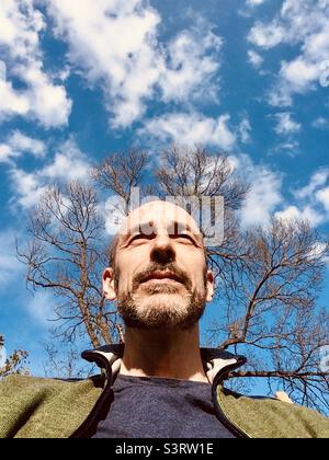 Ritratto uomo di mezza età di fronte ad un albero e cielo soleggiato visto dalla prospettiva della rana Foto Stock