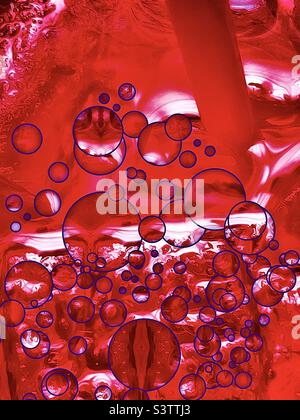Guardando giù in una tazza grande dello Sprite freddo della ciliegia del ghiaccio. Le bollicine viola sono state aggiunte digitalmente alla bevanda rossa, alla paglia e ai cubetti di ghiaccio per fare un astratto rinfrescante. Foto Stock