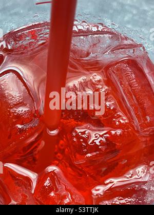 Guardando giù in una tazza grande dello Sprite freddo della ciliegia del ghiaccio. Il liquido carbonato rosso freddo, la paglia e il ghiaccio fanno un per un grande abstract rinfrescante. Foto Stock