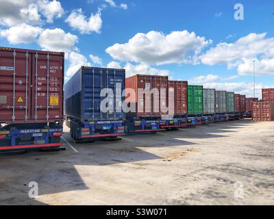 Una fila di rimorchi per camion parcheggiati in un porto o terminal caricato con contenitori di spedizione dopo ritardi nelle importazioni e nelle esportazioni Foto Stock