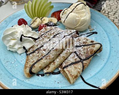 Piatto blu con crepes al cioccolato, frutta fresca e un cucchiaio di gelato alla vaniglia Foto Stock