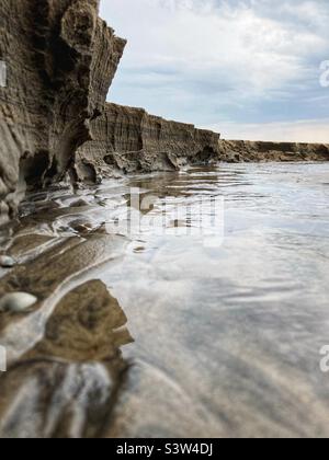 Primo piano della scarpa di un piccolo fiume che attraversa una spiaggia e che scorre nel Mar Baltico dando l'impressione di essere una grande scogliera, a soli 20 cm di altezza in realtà Foto Stock