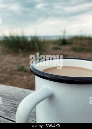 Un caffè con latte in una tazza di smalto bianco e nero su una tavola di legno sulla spiaggia della costa occidentale della Svezia Foto Stock