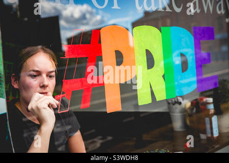 Ragazza dipingendo un segno bandiera arcobaleno Gay Pride sulla sua vetrina del negozio a sostegno della comunità gay Foto Stock