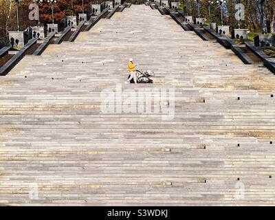 Giovane donna in mantello giallo che cammina per scale nel parco Foto Stock