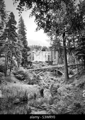 Vista della "bellezza dei cragside" dal torrente che guarda verso la passerella in ferro, la casa e i giardini di Cragside (bianco e nero) Foto Stock