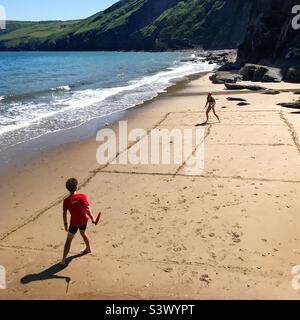 Madre e figlio giocano a tennis su una spiaggia appartata vicino a Llangrannog a Ceredigion, Galles. La marea sta arrivando e il campo da tennis improvvisato è disegnato a mano nella sabbia. Foto Stock