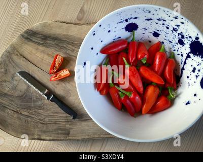 Preparandosi a tritare un peperoncino rosso su un asse di legno con una ciotola di peperoncini Foto Stock