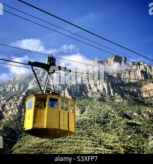 Una funivia turistica si dirige verso il monastero di Montserrat, vicino a Barcellona, in Catalogna, in Spagna, con le montagne nebbre alle spalle Foto Stock